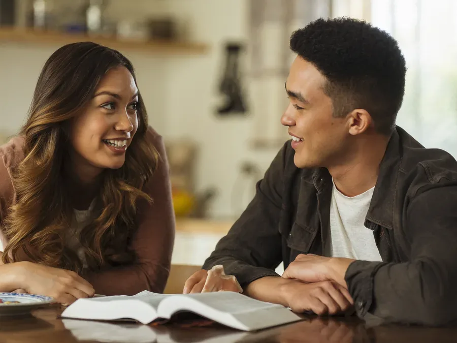 Two friends talking over an open Bible at a kitchen table